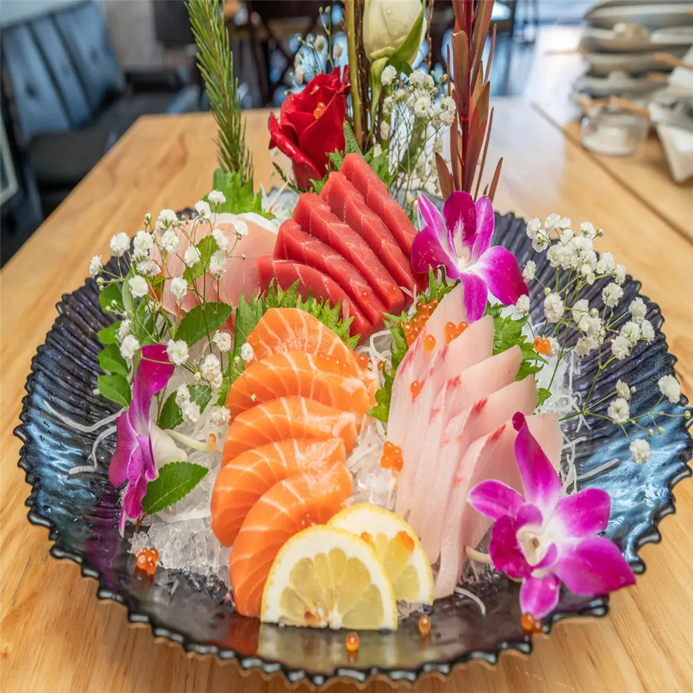 The Assorted Sashimi Platter showcases a variety of fresh raw fish, including salmon and tuna, artfully arranged with edible flowers and ice